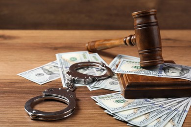 Judge's gavel, money and handcuffs on wooden table, closeup