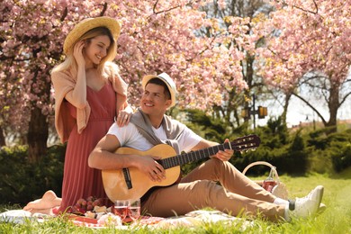 Happy couple with guitar having picnic in park on sunny day