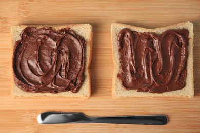 Photo of Tasty toasts with chocolate paste served on wooden board, flat lay