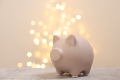 Photo of Piggy bank on grey table against blurred lights, space for text