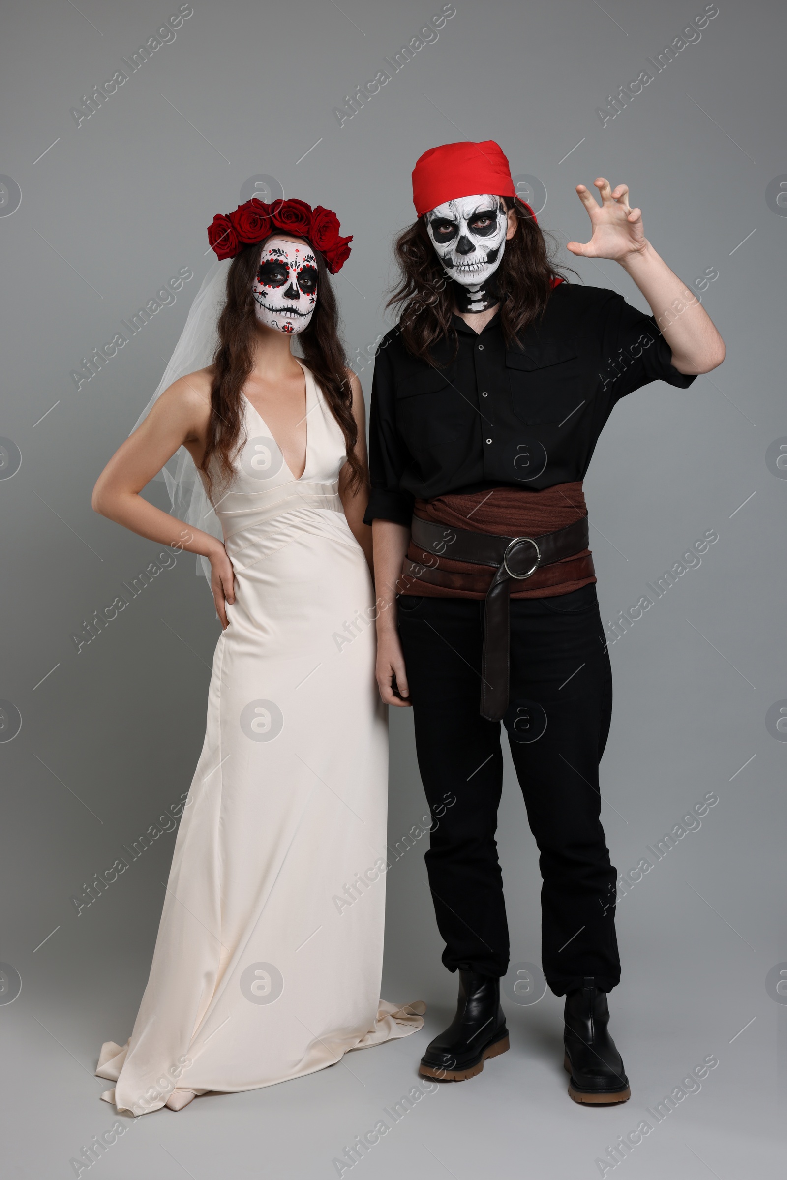 Photo of Couple in scary bride and pirate costumes on light grey background. Halloween celebration