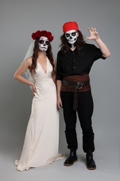 Photo of Couple in scary bride and pirate costumes on light grey background. Halloween celebration