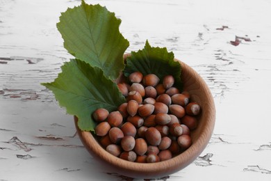 Photo of Bowl with hazelnuts and leaves on white wooden table