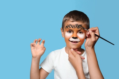 Photo of Artist painting face of little boy on blue background