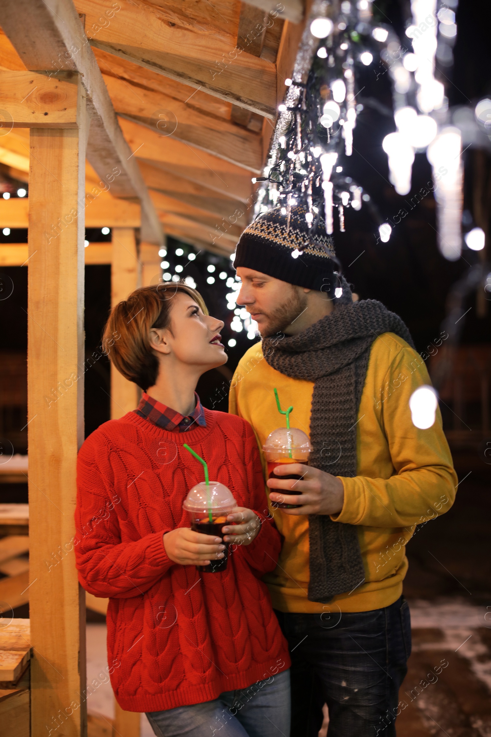 Photo of Young couple with cups of mulled wine at winter fair