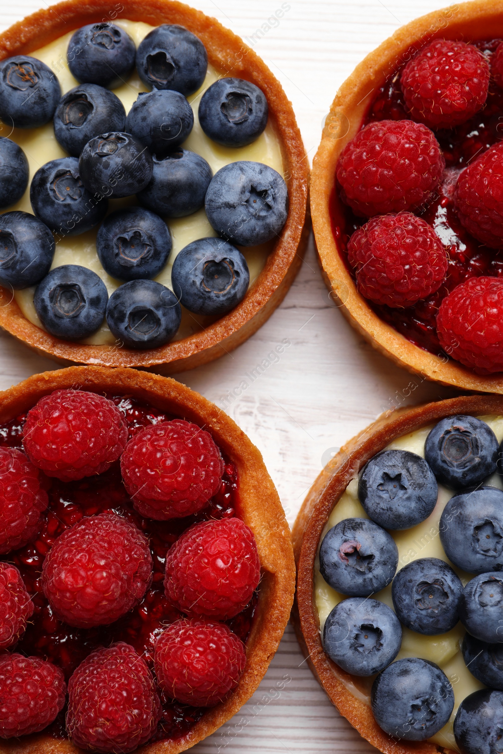 Photo of Tartlets with different fresh berries on white wooden table, flat lay. Delicious dessert