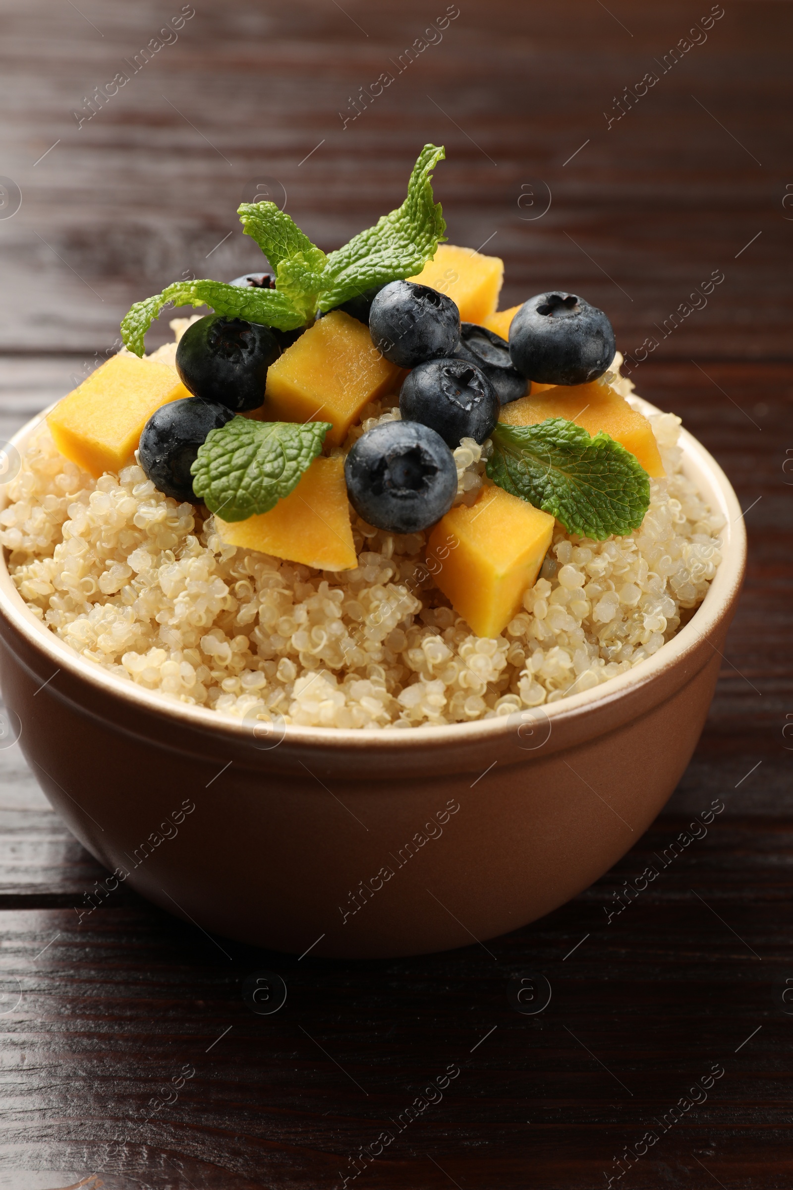 Photo of Tasty quinoa porridge with blueberries, pumpkin and mint in bowl on wooden table, closeup