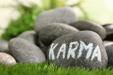Stone with word Karma on green grass, closeup. Space for text