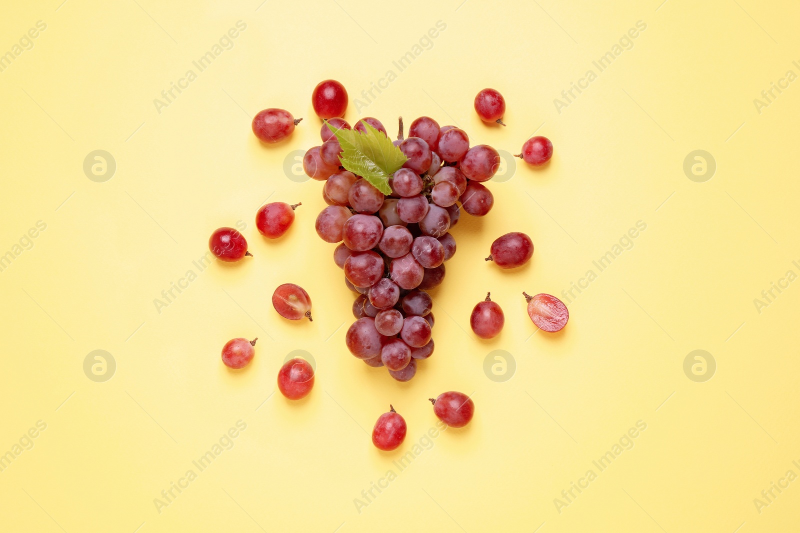 Photo of Bunch of ripe red grapes with green leaf on yellow background, flat lay