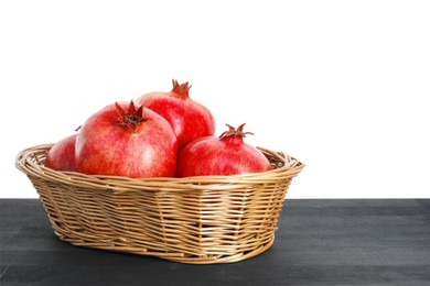 Photo of Fresh pomegranates in wicker basket on black wooden table against white background, space for text