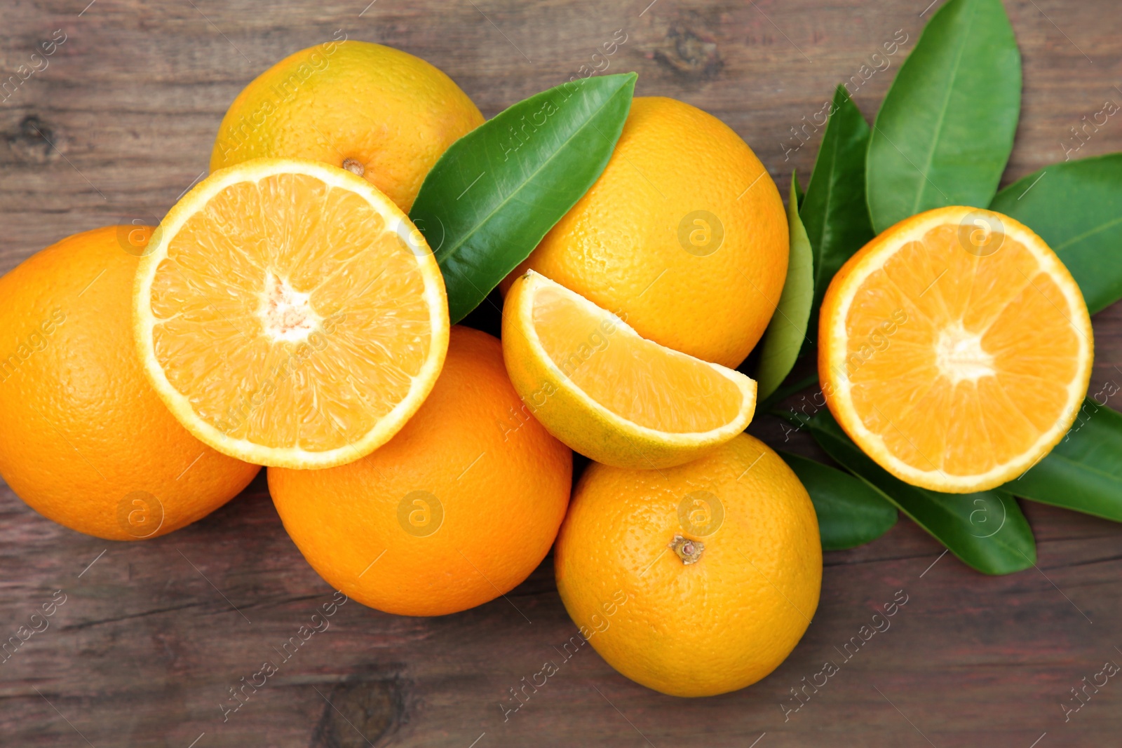 Photo of Many ripe oranges and green leaves on wooden table, flat lay