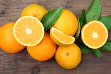 Photo of Many ripe oranges and green leaves on wooden table, flat lay