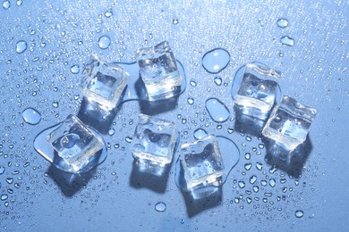 Melting ice cubes and water drops on blue background, flat lay