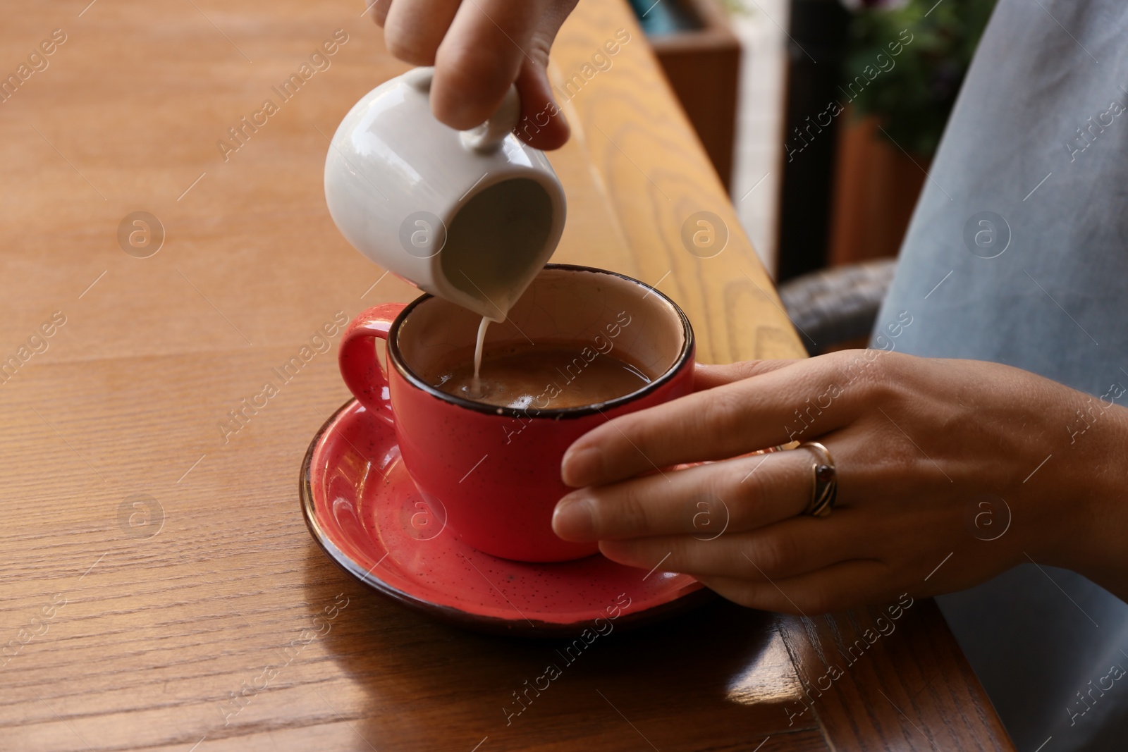 Photo of Woman adding milk to fresh aromatic coffee at table, closeup