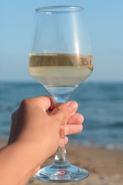 Woman holding glass of tasty wine near sea, closeup