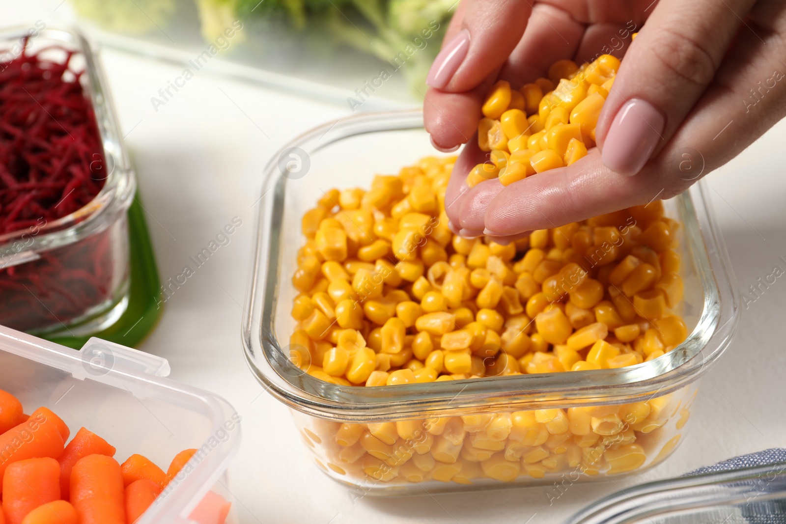 Photo of Woman putting corn into glass container at white table, closeup. Food storage