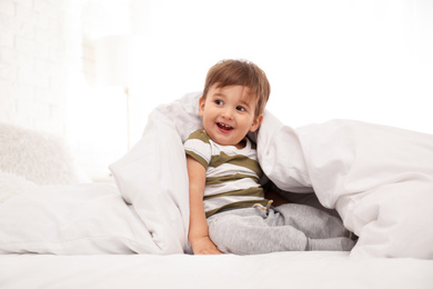 Photo of Cute little child playing under blanket in bed