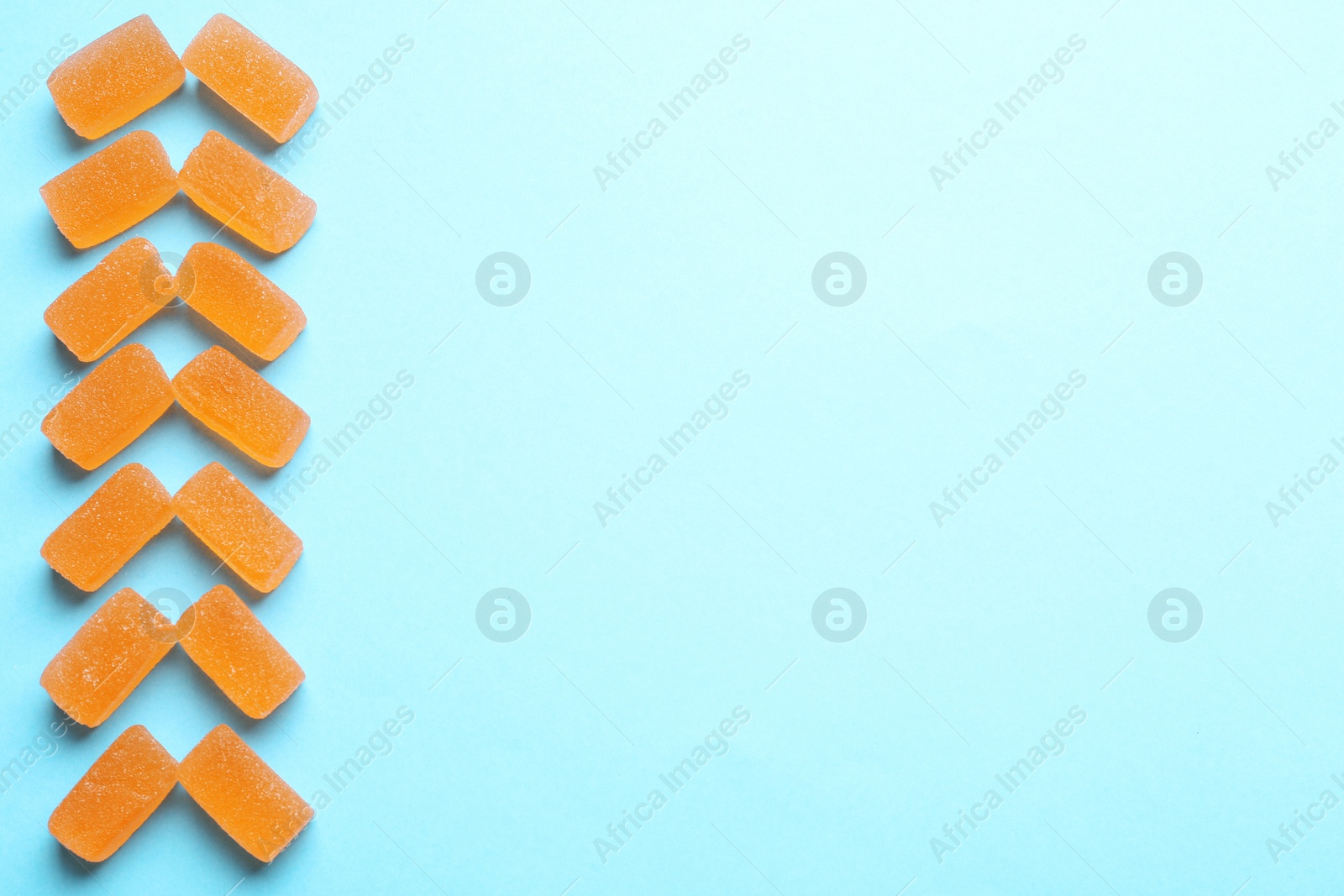 Photo of Tasty orange jelly candies on turquoise background, flat lay. Space for text