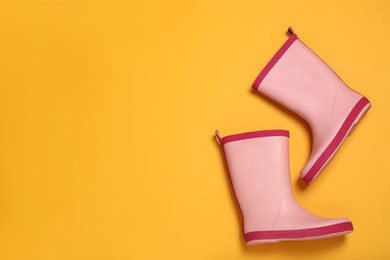 Photo of Pink rubber boots on yellow background, flat lay. Space for text