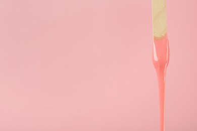 Wooden spatula with hot depilatory wax on pink background. Space for text