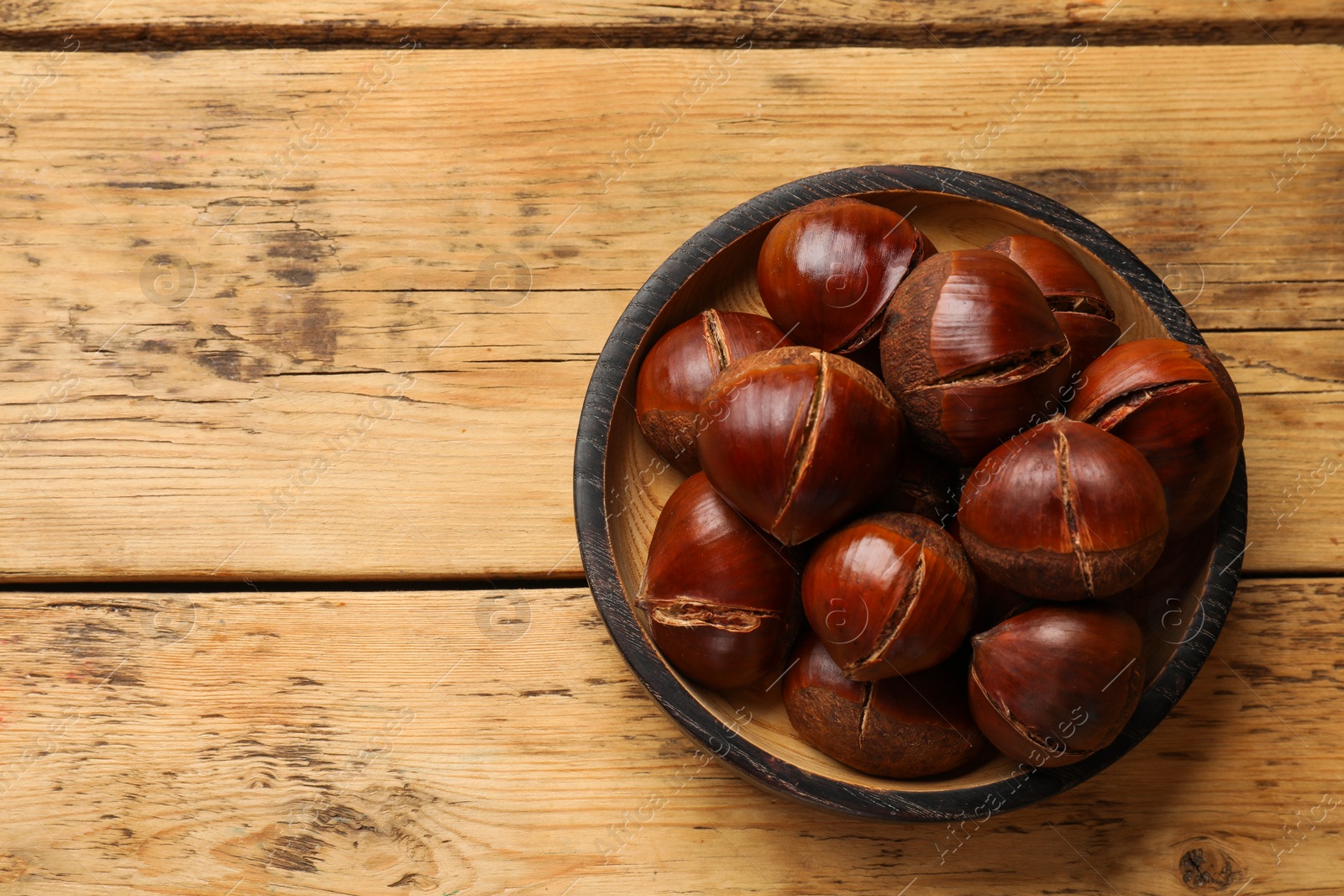 Photo of Fresh edible sweet chestnuts in bowl on wooden table, top view. Space for text