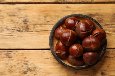 Fresh edible sweet chestnuts in bowl on wooden table, top view. Space for text