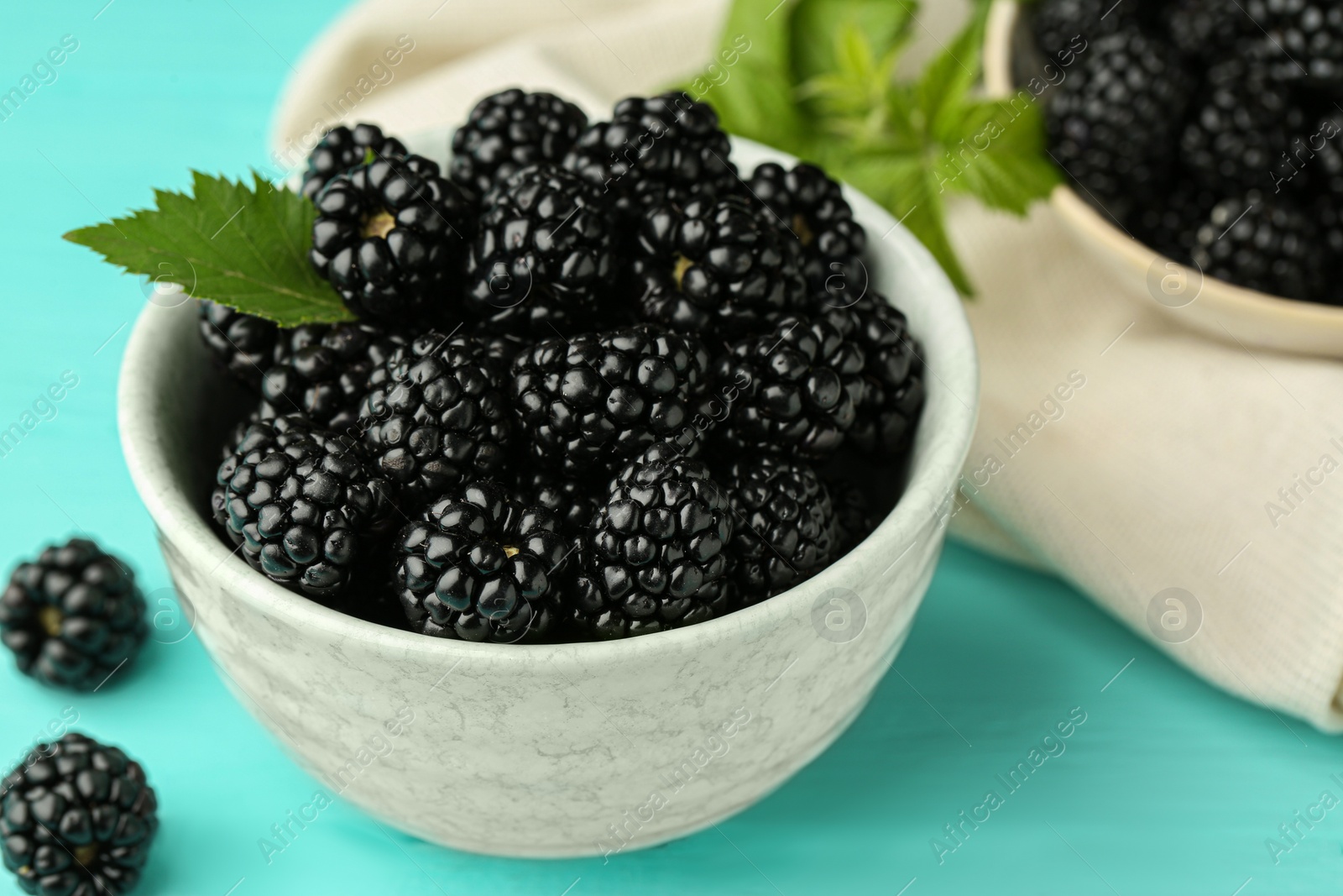 Photo of Bowl of fresh ripe blackberries on turquoise wooden table, closeup