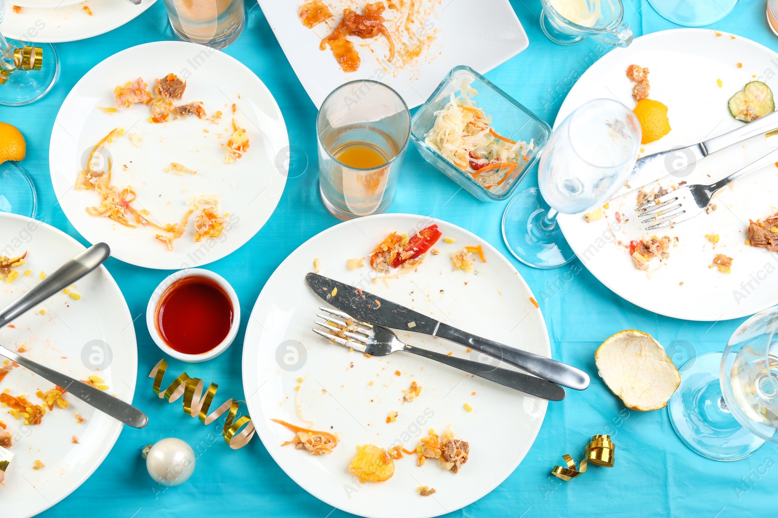 Photo of Dirty tableware with leftovers on light blue cloth after party