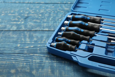 Photo of Set of screwdrivers in open toolbox on blue wooden table, closeup. Space for text