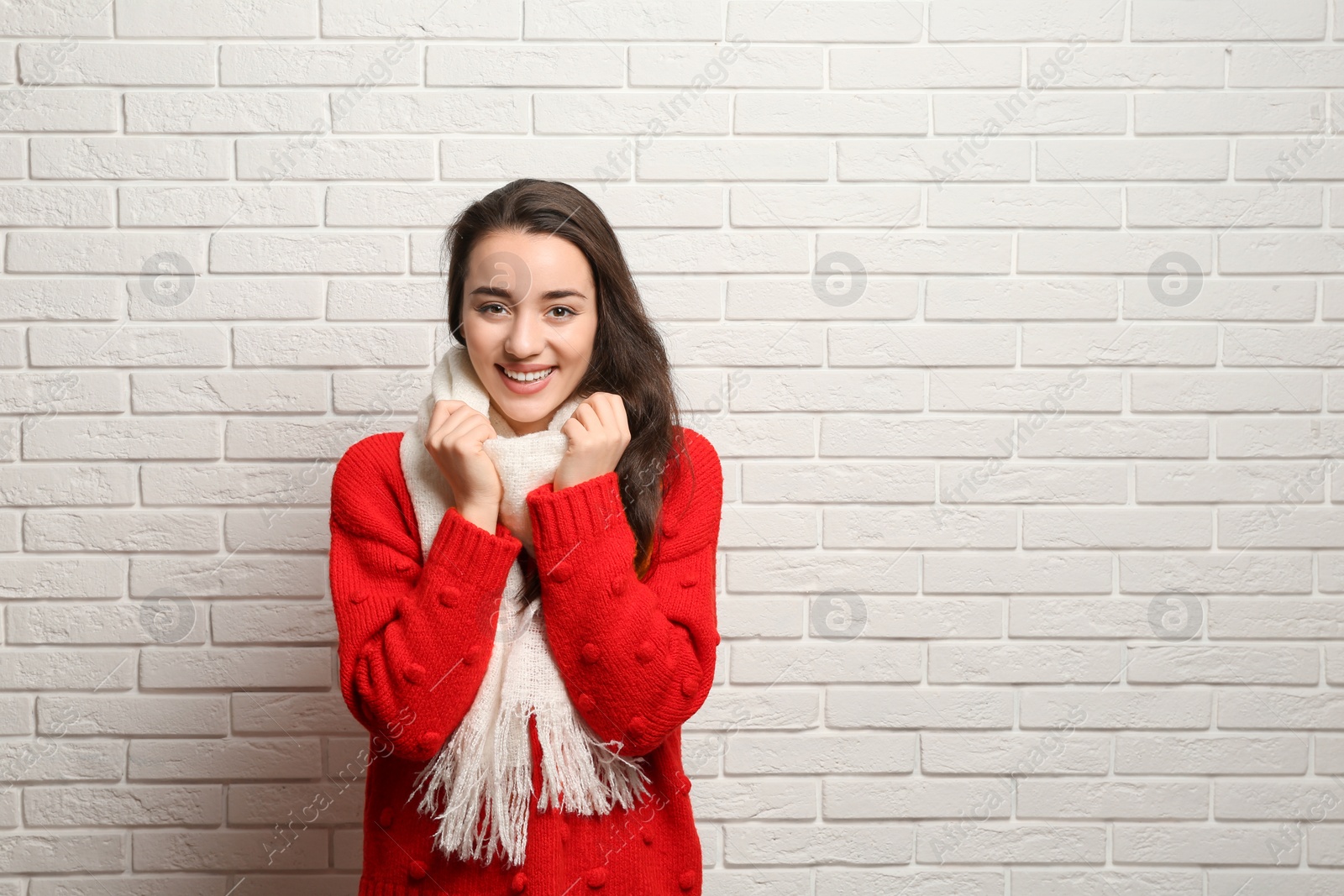 Photo of Young woman wearing warm clothes near brick wall, space for text. Winter season