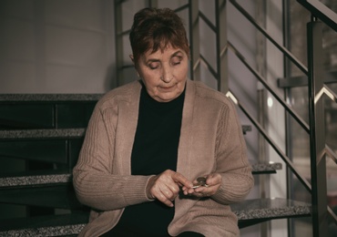 Photo of Poor senior woman with coins sitting on stairs indoors