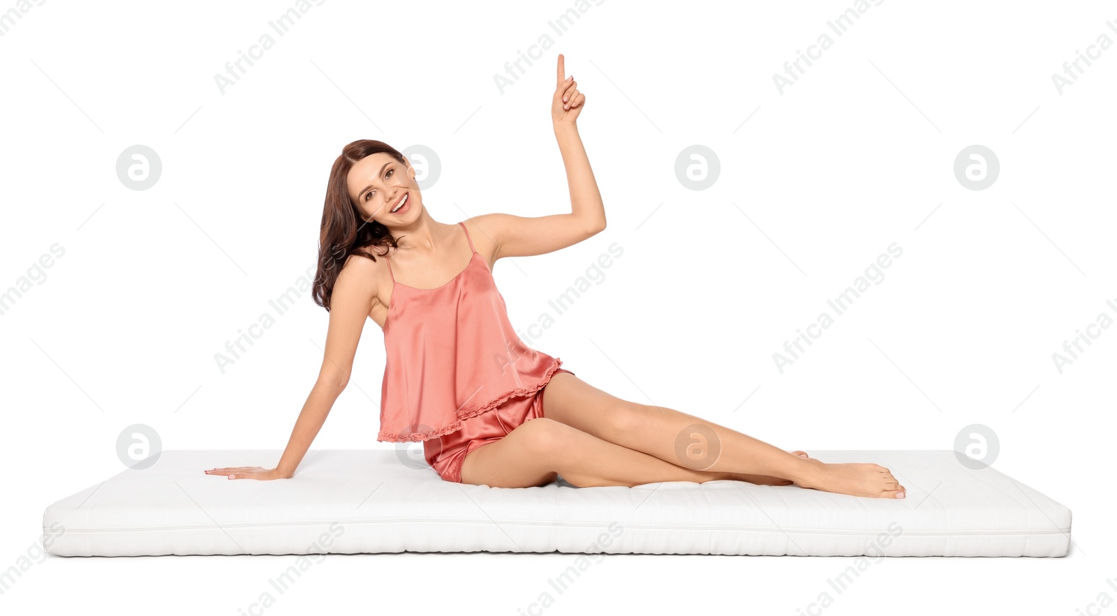 Photo of Young woman sitting on soft mattress and pointing upwards against white background