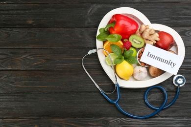 Card with word Immunity, stethoscope and fresh products on dark wooden table, flat lay. Space for text