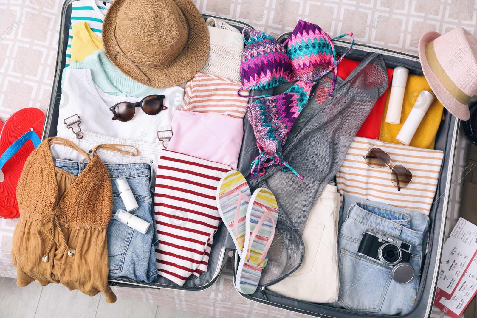 Photo of Open suitcase with summer clothes, accessories and shoes on bed, flat lay
