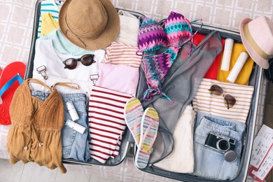 Open suitcase with summer clothes, accessories and shoes on bed, flat lay