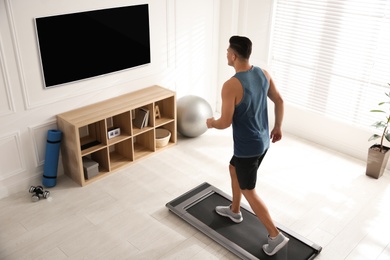 Sporty man training on walking treadmill while watching TV at home