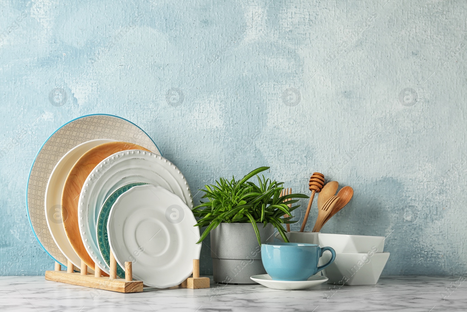 Photo of Green plant and different kitchenware on table near color wall. Modern interior design