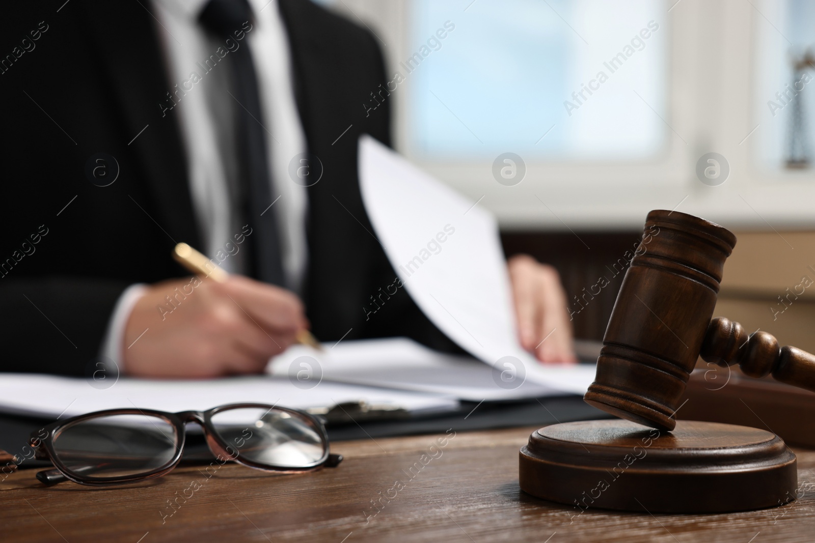 Photo of Lawyer working with documents at wooden table in office, focus on gavel