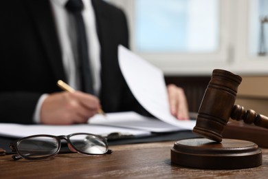 Photo of Lawyer working with documents at wooden table in office, focus on gavel