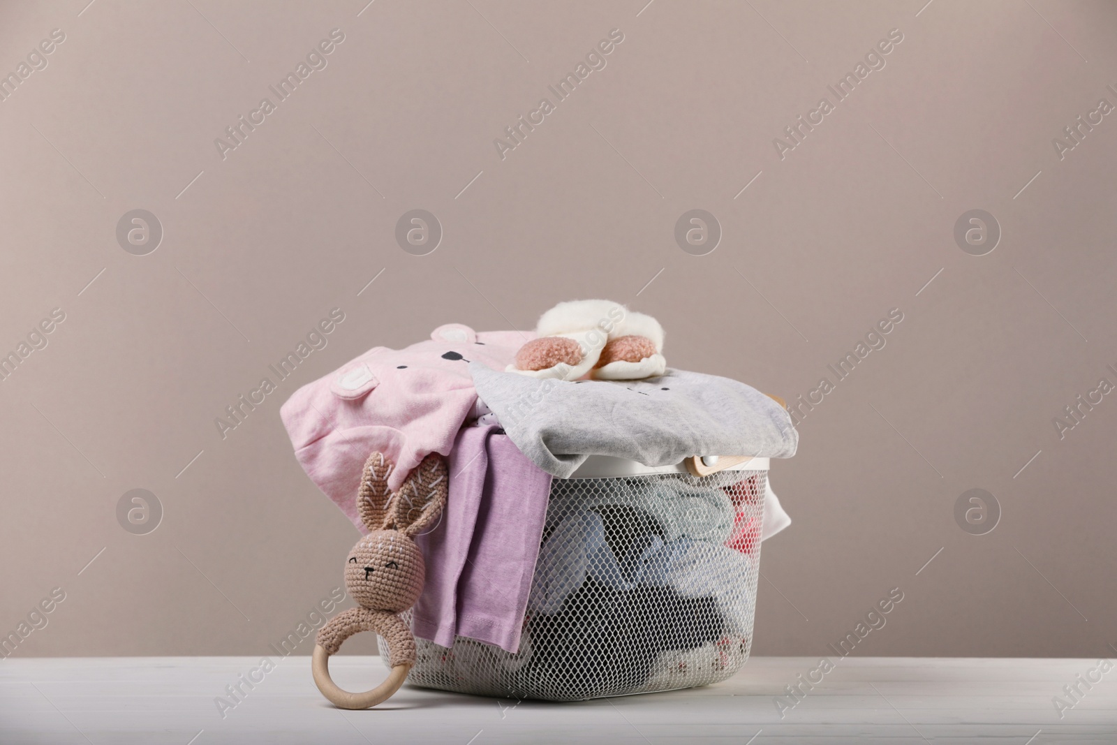 Photo of Laundry basket with baby clothes and toy on white wooden table