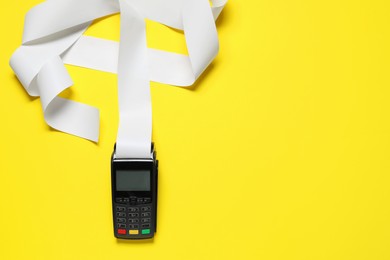 Photo of Payment terminal with thermal paper for receipt on yellow background, top view. Space for text