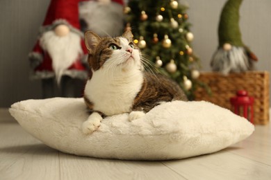 Photo of Cute cat lying on soft pillow near Christmas decor at home. Adorable pet