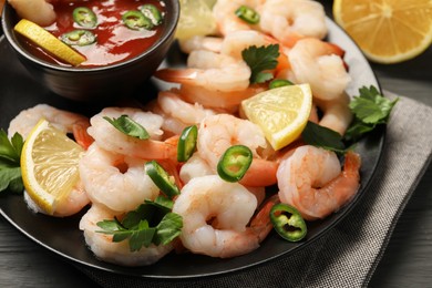 Photo of Tasty boiled shrimps with cocktail sauce, chili, parsley and lemon on table, closeup