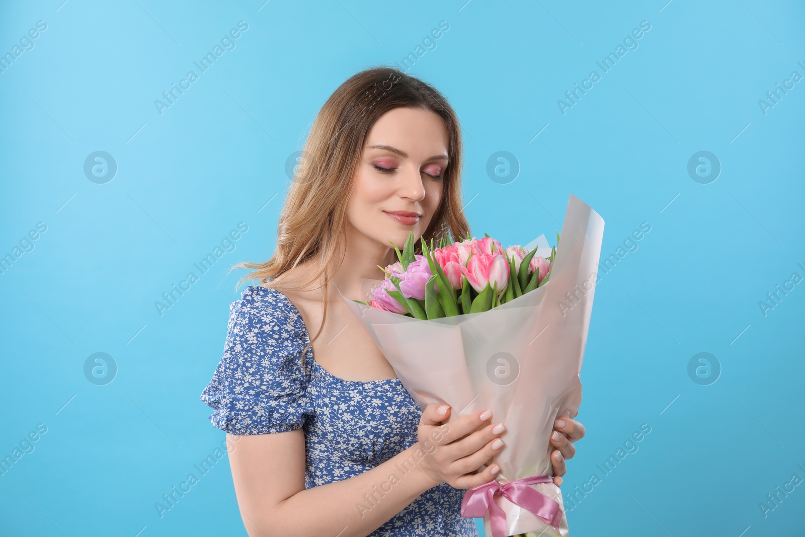 Photo of Happy young woman with bouquet of beautiful tulips on light blue background