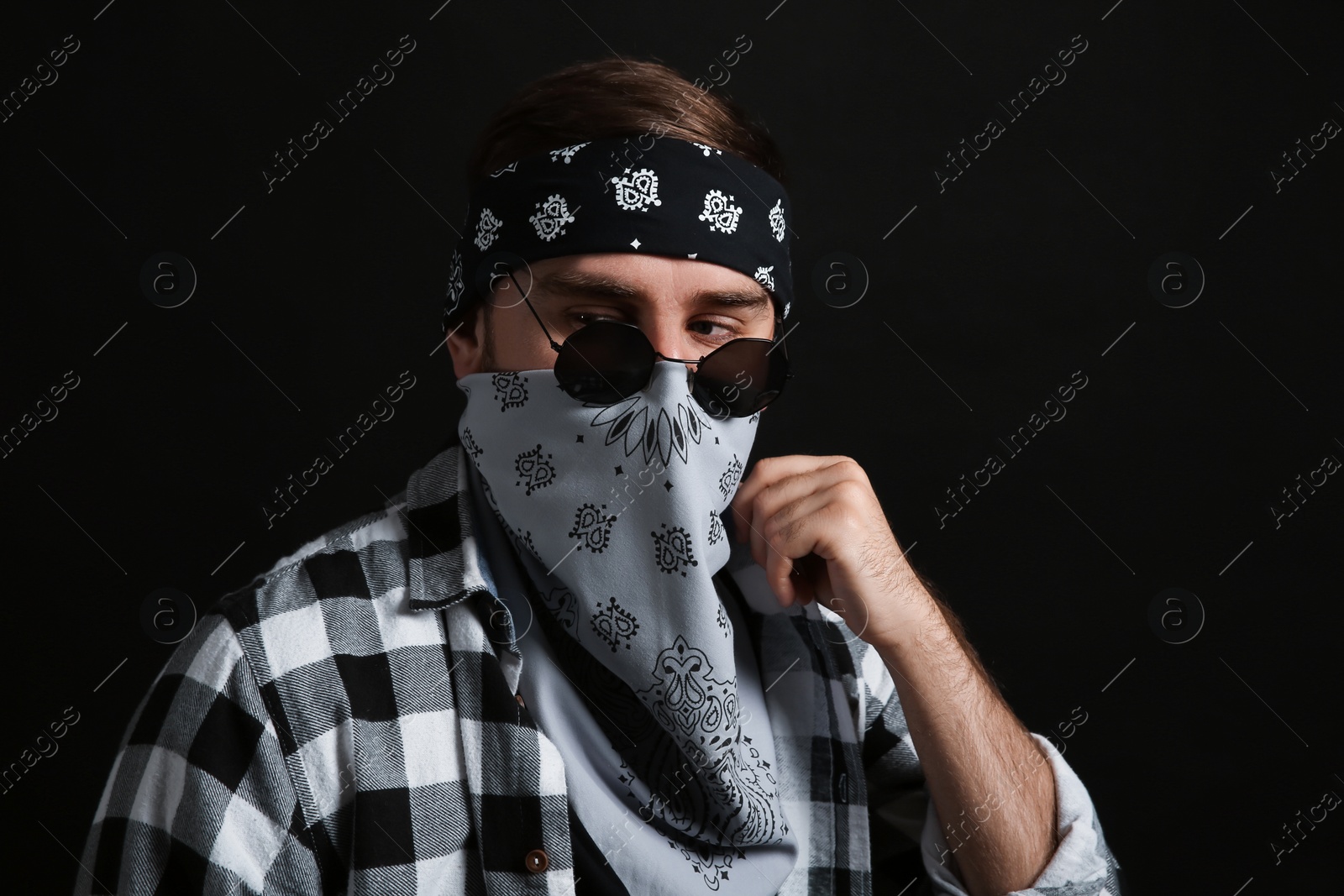 Photo of Fashionable young man with bandana covering his face on black background