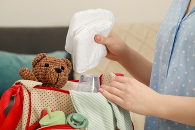 Photo of Woman putting diapers into mother`s bag indoors, closeup