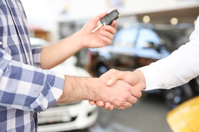 Photo of Young man shaking hands with salesman in car salon