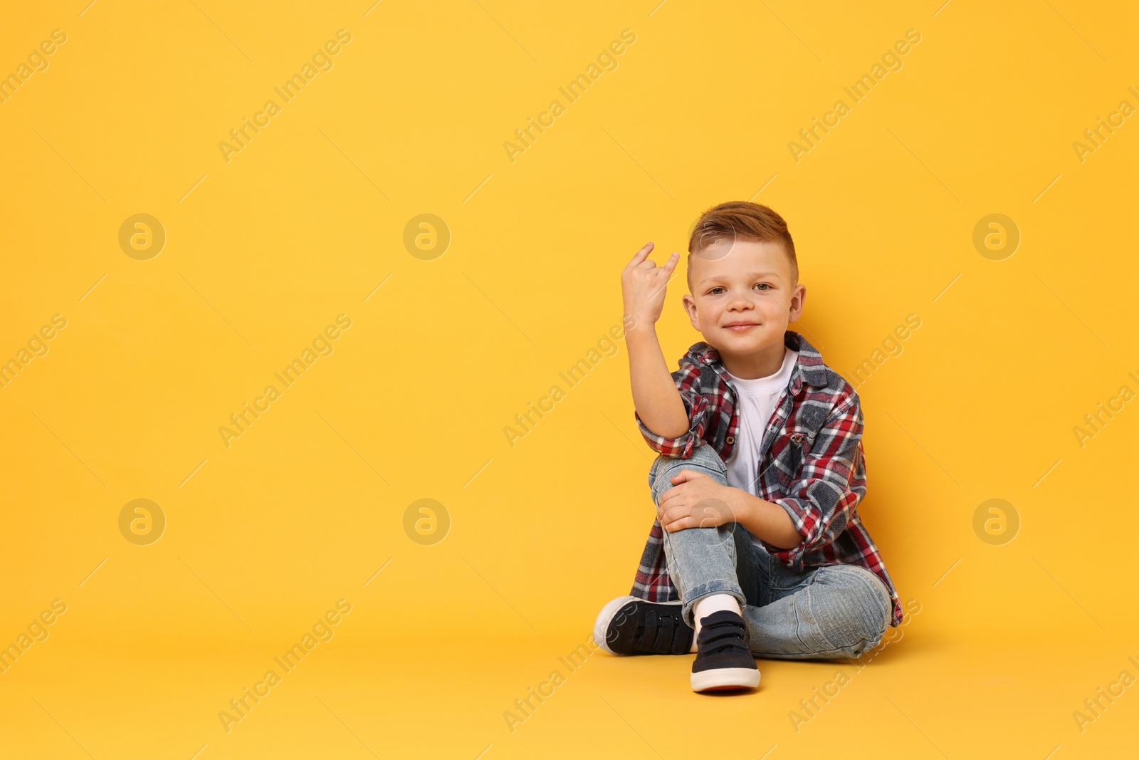 Photo of Happy little boy sitting on yellow background. Space for text