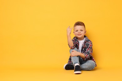 Photo of Happy little boy sitting on yellow background. Space for text