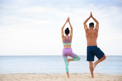 Couple practicing yoga on beach, back view with space for text. Body training